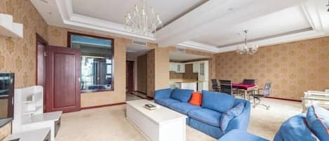 A spacious living room with a large blue sofa, a white coffee table, and a chandelier.