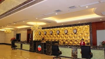 A hotel reception area with a marble floor, a reception desk, and a chandelier.