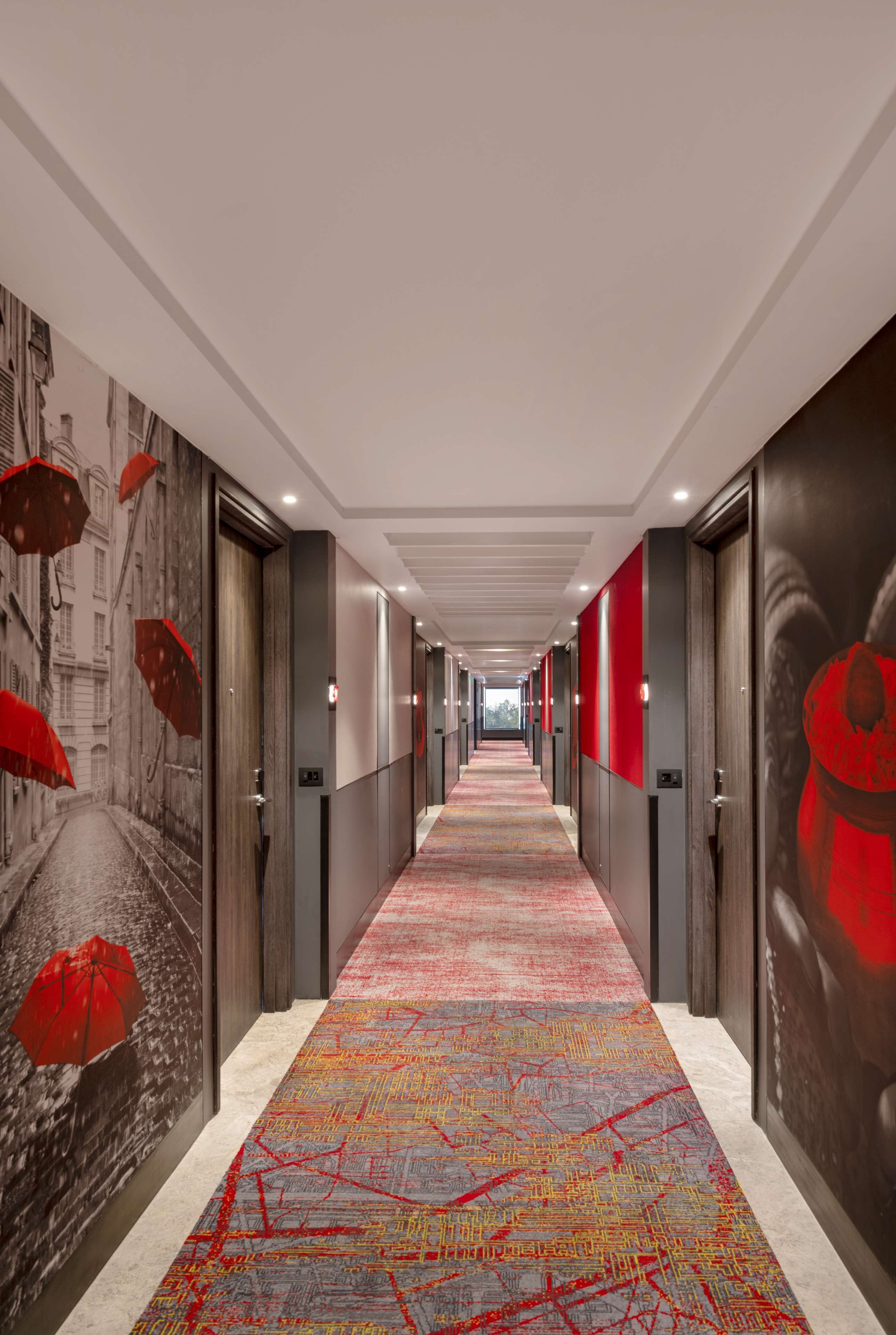 A hallway with a patterned carpet, doors with red accents, and a mural on the walls.