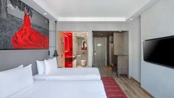 Una habitación de hotel moderna con una cama grande, un televisor y un banco rojo.