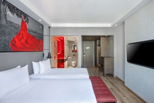 Una habitación de hotel moderna con una cama grande, un televisor y un banco rojo.