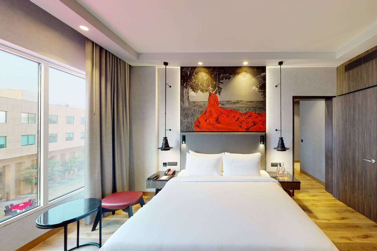 A hotel room with a large bed, a desk, a chair, and a window with a view of buildings.