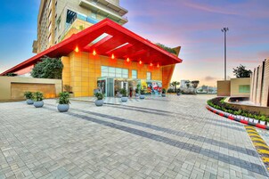 Un edificio moderno con un alero rojo, ventanas amplias y un acceso pavimentado con plantas en macetas.