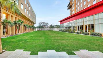 Un patio con césped verde, palmeras y un edificio rojo con ventanas amplias.