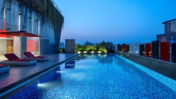 A rooftop swimming pool with lounge chairs and a view of the city skyline at dusk. - Radisson Red Chandigarh Mohali (Mohali)
