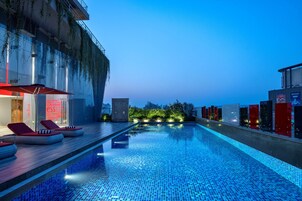 Una piscina en la azotea con sillones de descanso y vistas del horizonte urbano al anochecer.
