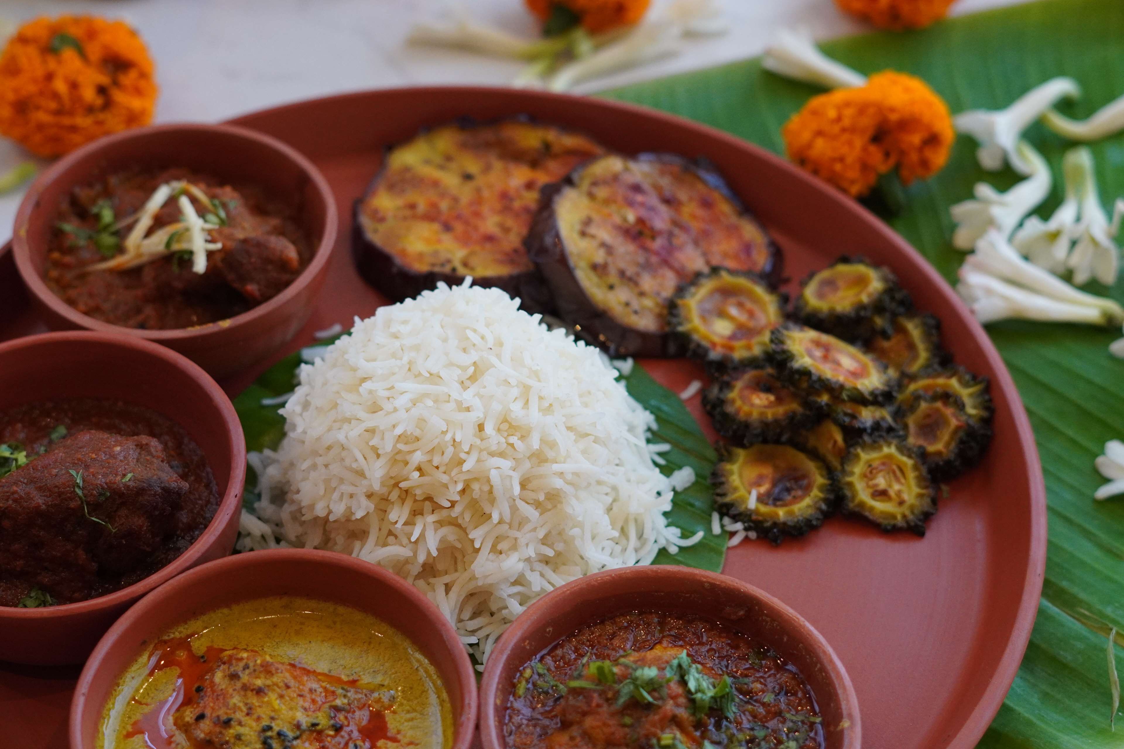 A traditional Indian meal with rice, various curries, and grilled vegetables on a banana leaf.