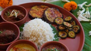 A traditional Indian meal with rice, various curries, and grilled vegetables on a banana leaf.