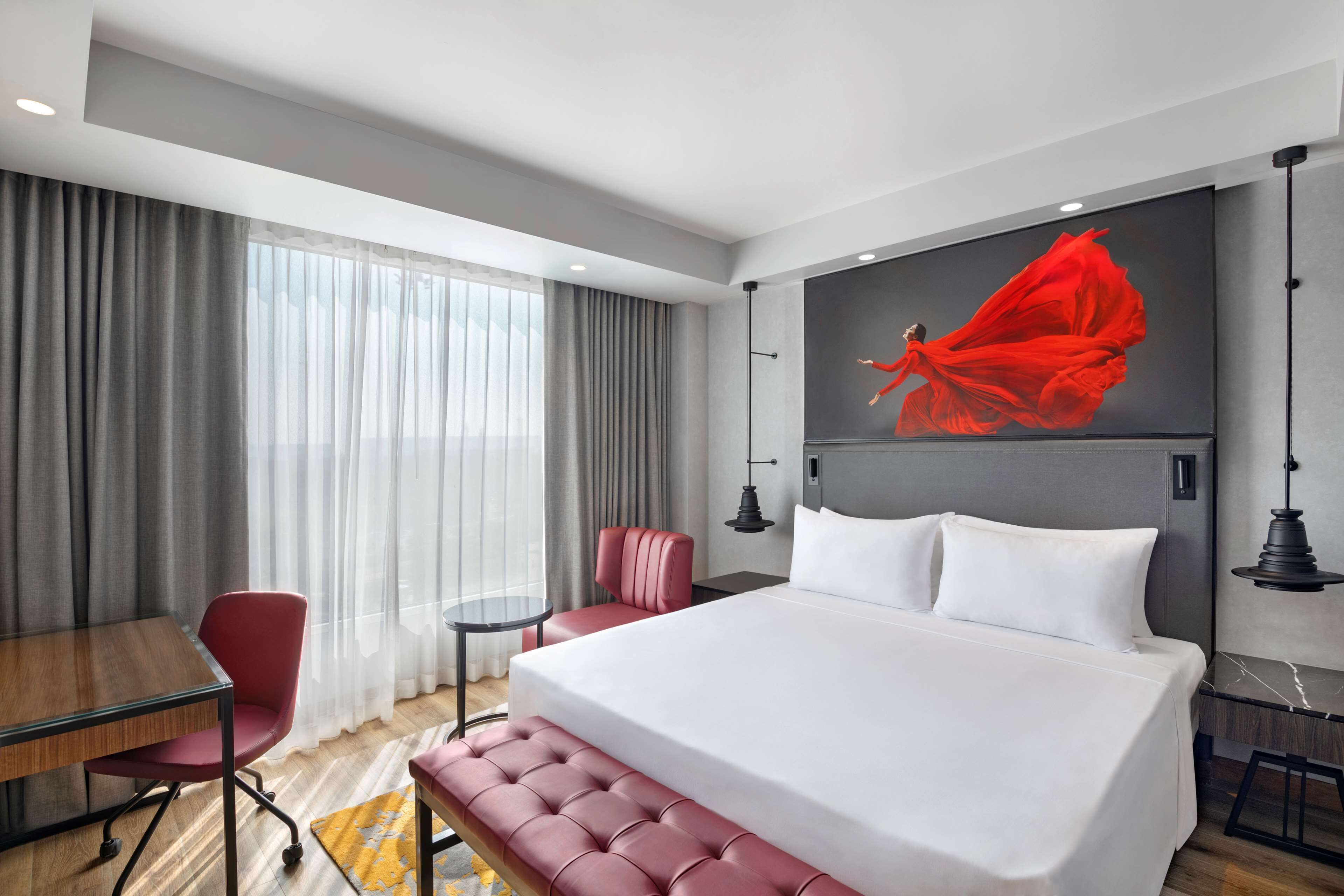 A modern hotel room with a large bed, a desk, a chair, and a small table.