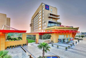 Un hotel moderno con un llamativo letrero ROJO, un acceso ajardinado y una zona de piscina.