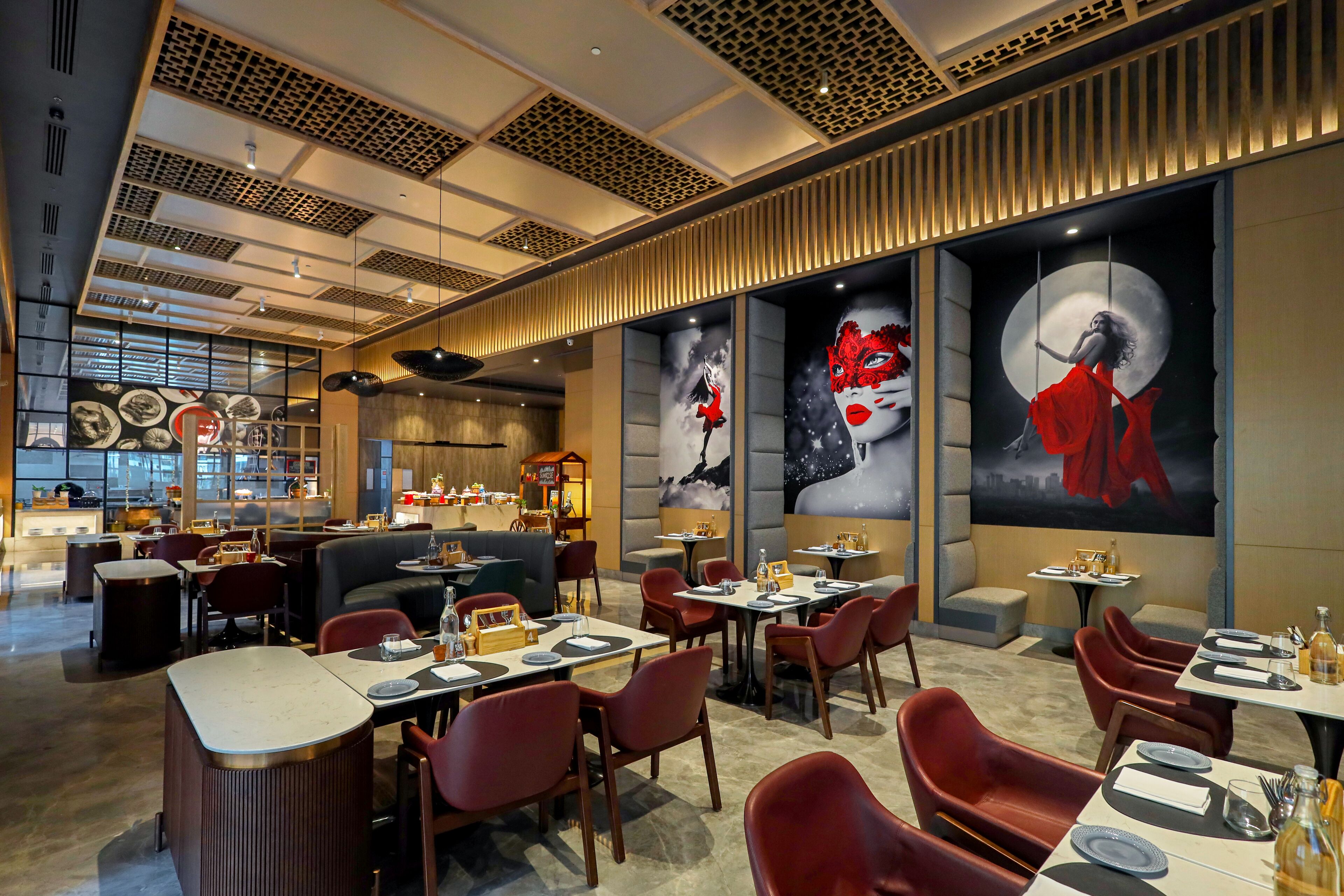 Un restaurant moderne avec de hauts plafonds, un décor orné au plafond et de grandes fenêtres. Les tables et les chaises sont disposées pour accueillir les clients.