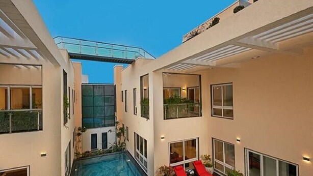 A modern building with a central swimming pool, multiple balconies, and outdoor seating areas. - Maroma Suites (Chennai)