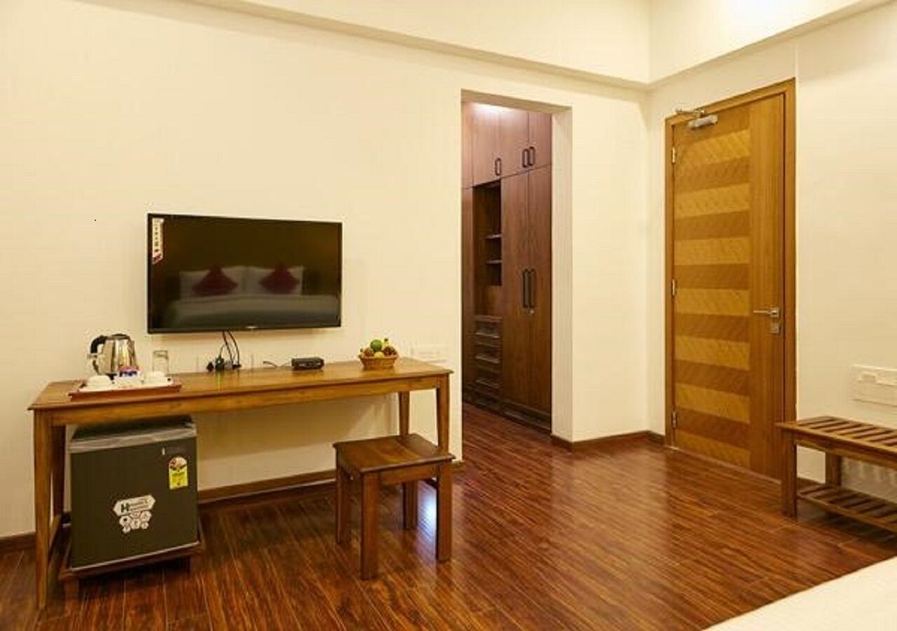 Una habitación compacta con escritorio de madera, televisión, refrigerador pequeño y armario.