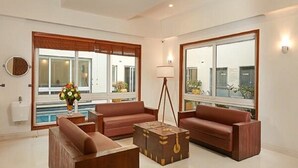 A spacious living room with a large window, a sofa, a coffee table, and a lamp. - Maroma Suites (Chennai)