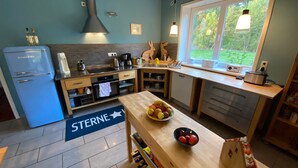 Une cuisine moderne avec un réfrigérateur bleu, une cuisinière et une fenêtre donnant sur un jardin.