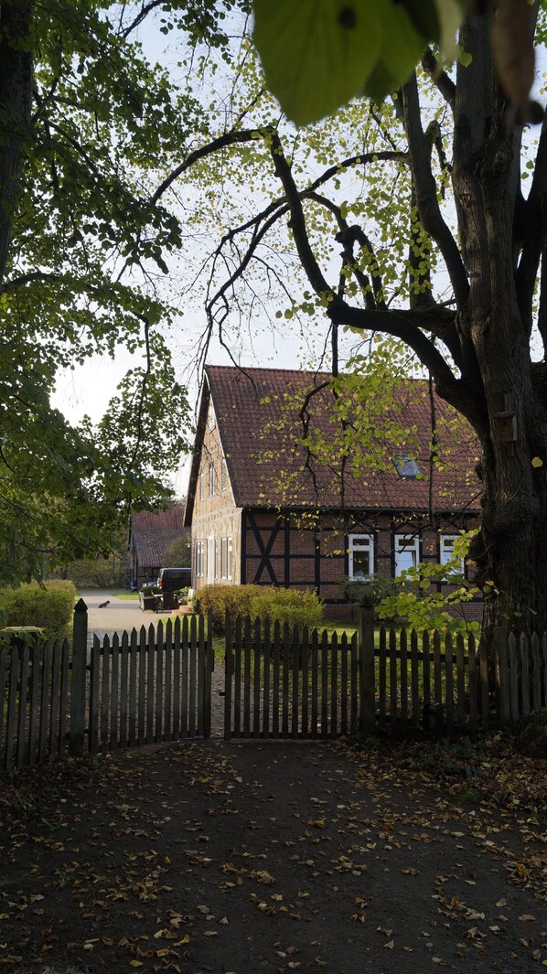 A traditional half-timbered house with a sloped roof, surrounded by a wooden fence and a paved driveway.