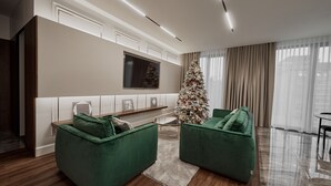 Una sala de estar moderna con sofás verdes, un árbol de Navidad y un televisor de pantalla plana montado en la pared.