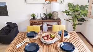 A dining table set with blue plates, white bowls, and fruits, surrounded by yellow chairs and a black bean bag.