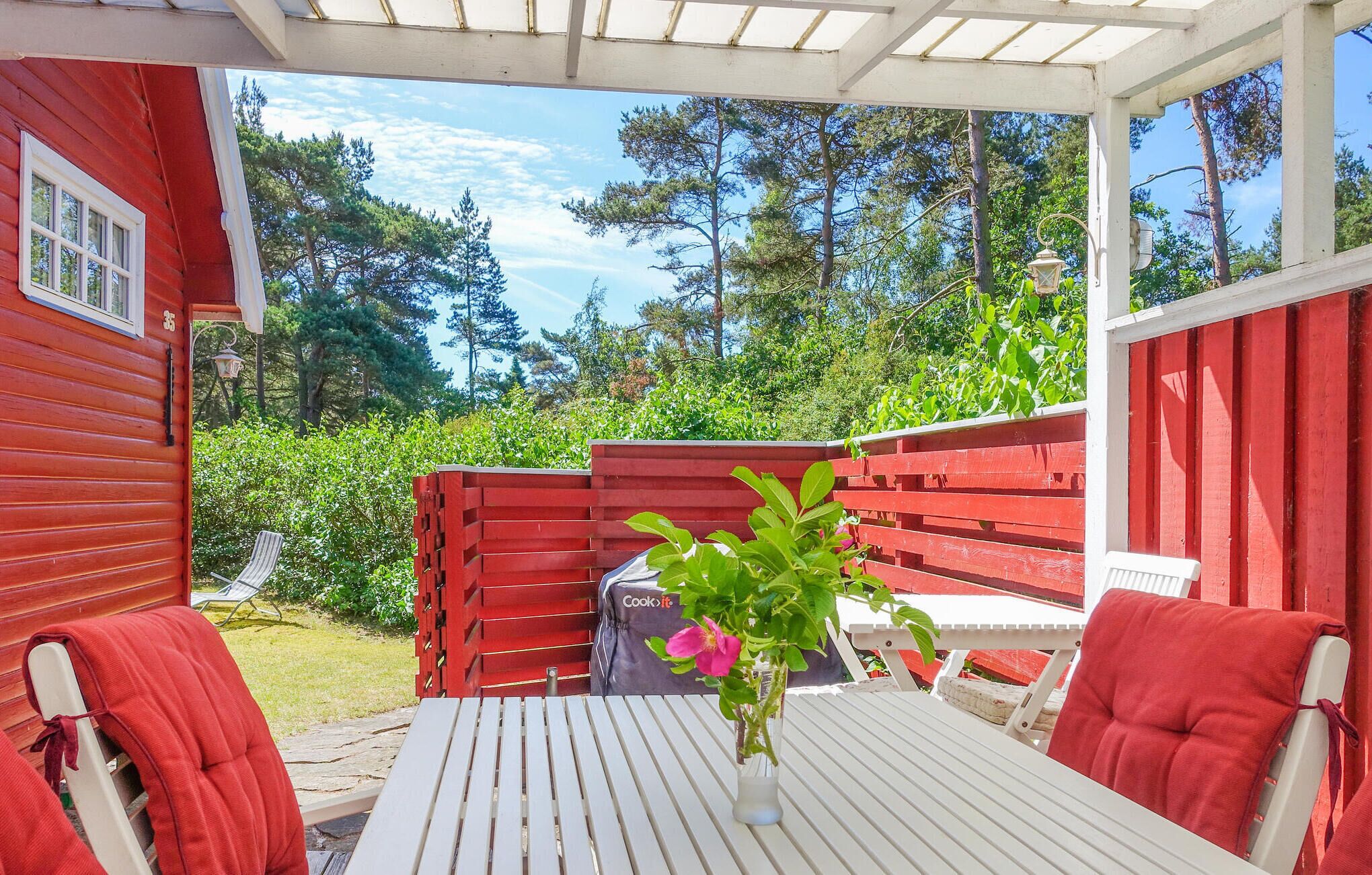 Une terrasse avec une table blanche et des chaises rouges, une clôture rouge et une vue sur les arbres et la verdure.