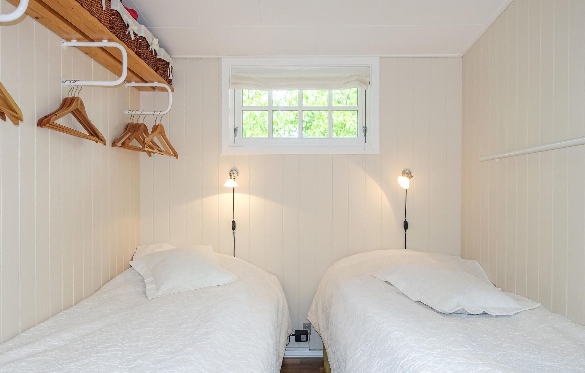 A bedroom with two beds, a window, and a wooden shelf with clothes.