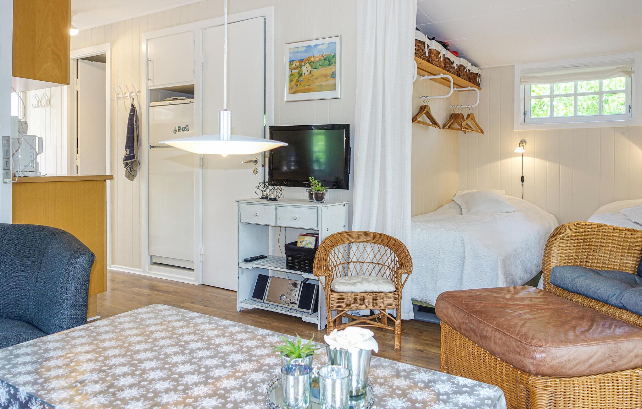 Un salon chaleureux avec un téléviseur, des meubles en osier et un coin repas agrémenté d’une nappe à motifs floraux.