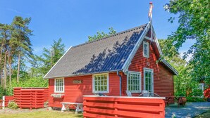A red wooden cabin with a steeply pitched roof, a chimney, and a small porch area with a bench. - 1 bedroom stunning home in Nexø (Nexø)