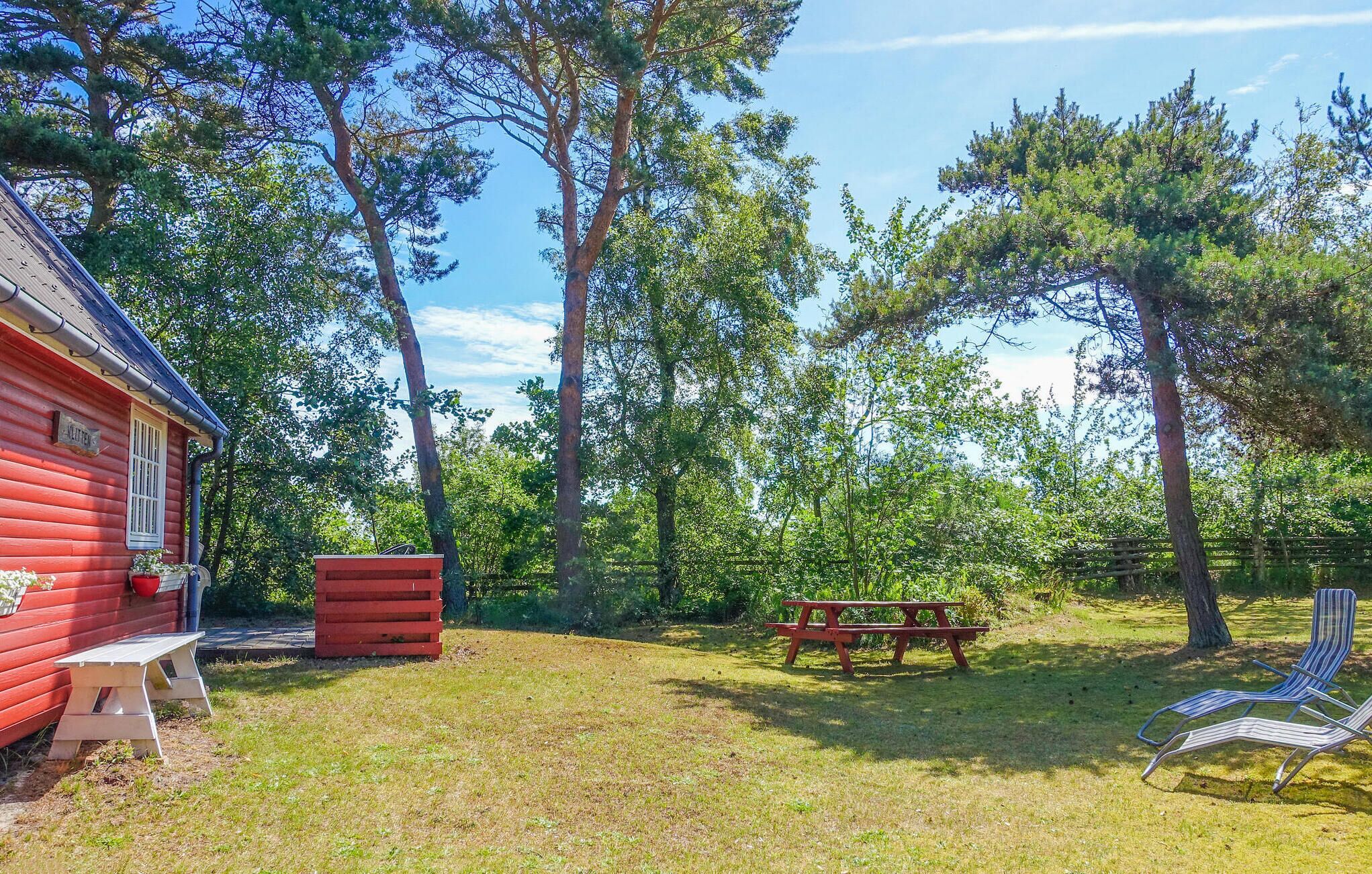 A red cabin with a picnic table and chairs in a wooded area.