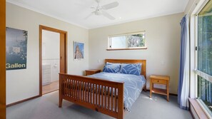 A bedroom with a wooden bed, a nightstand, a ceiling fan, a window with curtains, and a poster on the wall. - Breeze on Scenic - 7 Scenic Way, Carrickalinga (Carrickalinga)