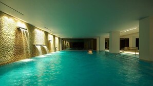 Une grande piscine intérieure avec un mur texturé d’un côté et un mur de verre de l’autre.