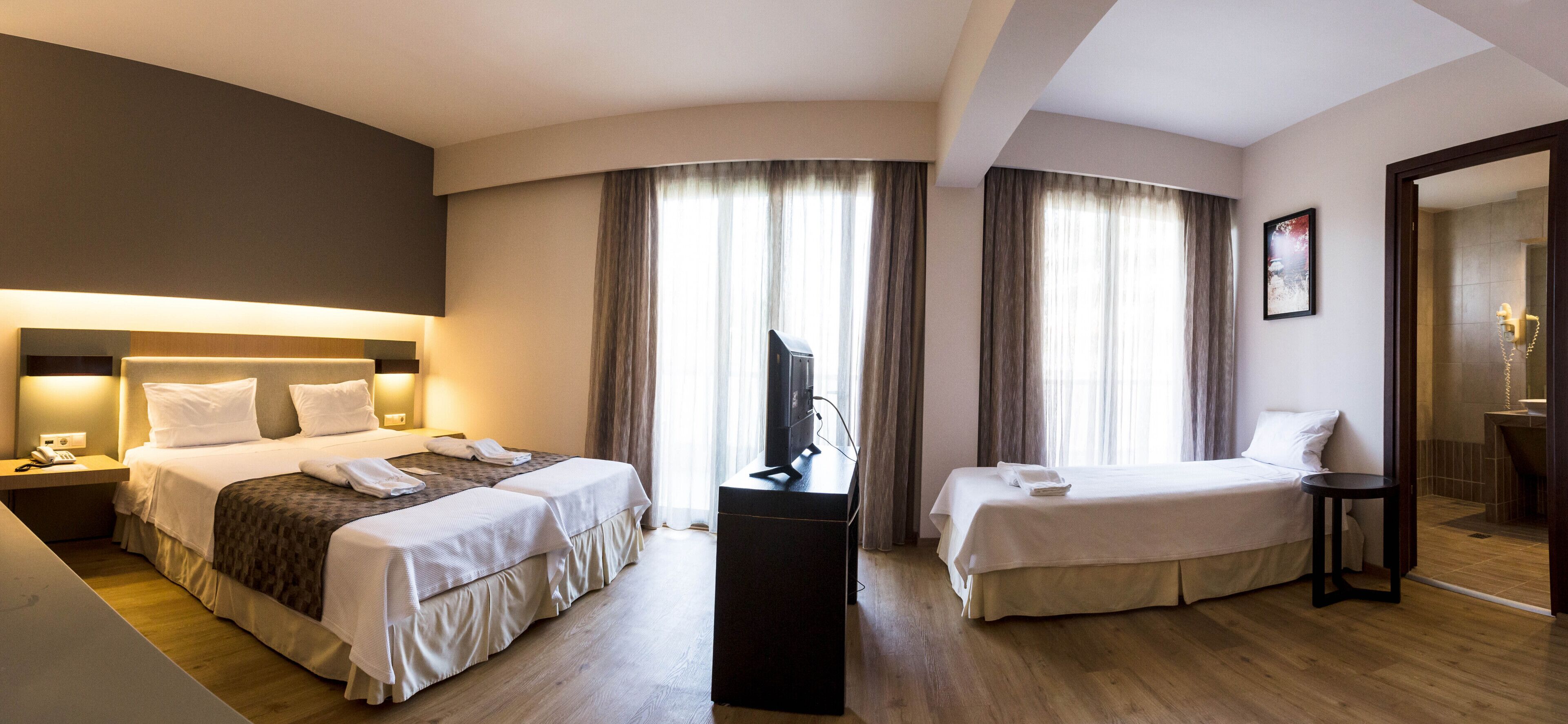 A hotel room with two beds, a desk, a chair, and a TV.