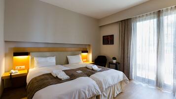 Habitación de hotel con una cama grande, mesitas de noche, una silla, una pequeña mesa con una planta y una ventana con cortinas.