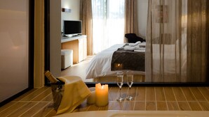 Une chambre d’hôtel avec un lit, une télévision, un bureau, une chaise, une bouteille de champagne, deux verres et une bougie.