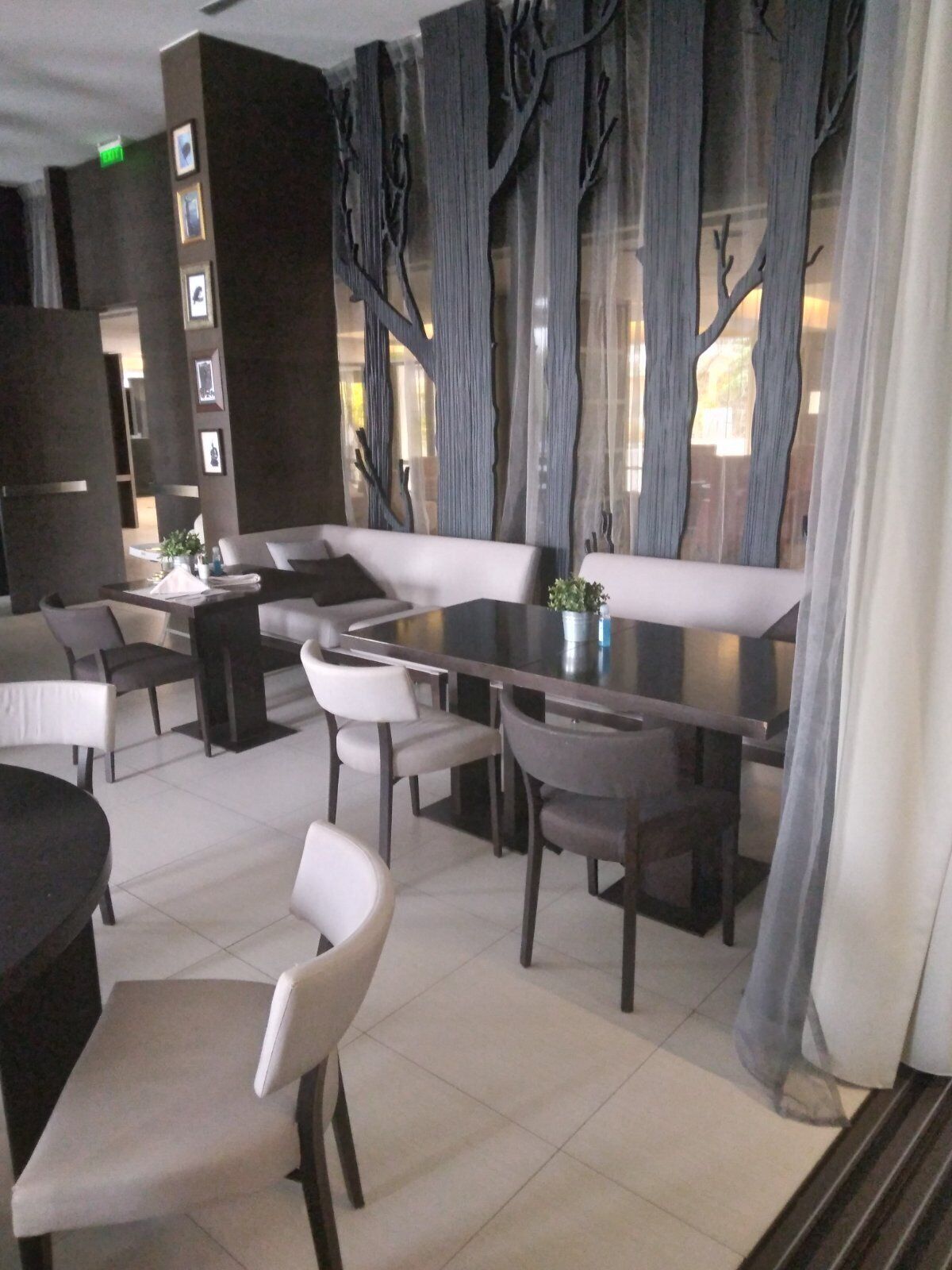Un comedor moderno con una mesa larga, varias sillas y un banco. Hay cuadros en la pared y una ventana con cortinas.