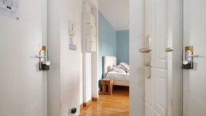 Een gang die leidt naar een slaapkamer met een bed, nachtkastje en een telefoon aan de muur.