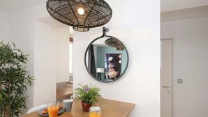 Een eethoek met een ronde spiegel, een tafel met ontbijtartikelen, een potplant en een hanglamp.