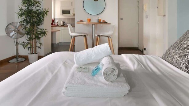 Een hotelkamer met een bed, een eettafel met stoelen, een hanglamp en een kamerplant.