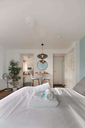 Une chambre d’hôtel avec un lit, une table à manger avec des chaises, un luminaire suspendu et une plante en pot.