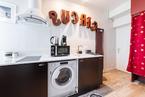 A compact kitchen with a washing machine, a microwave, and a coffee maker on the counter.