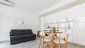 Eine moderne Küche mit weißen Schränken, einem Esstisch mit Stühlen und einem schwarzen Sofa.