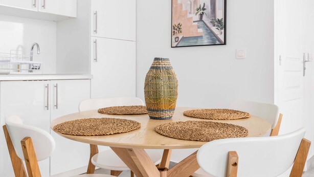 Eine moderne Küche mit weißen Schränken, einem Holzespeisetisch mit vier Stühlen und einer dekorativen Vase.