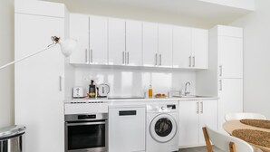 Eine moderne Küche mit weißen Schränken, einem Einbauofen, einer Waschmaschine und einem Essbereich mit Tisch und Stühlen.