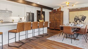 Una cocina moderna con armarios blancos, techo de madera y un comedor con mesa y sillas.