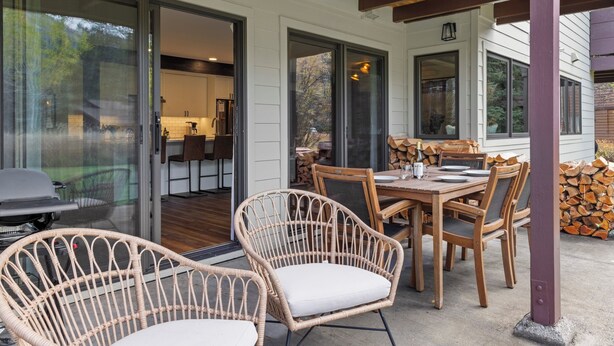 Un patio exterior con sillas de mimbre y una mesa de comedor, conectado a una puerta de cristal que da a una cocina.