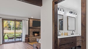 Un baño moderno con un espejo grande, lavamanos doble y chimenea de piedra.