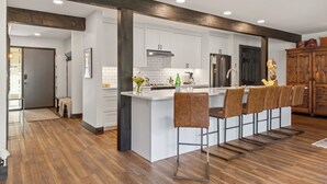 Una cocina moderna con armarios blancos, una isla central con taburetes y vigas de madera, además de un mueble de madera grande.