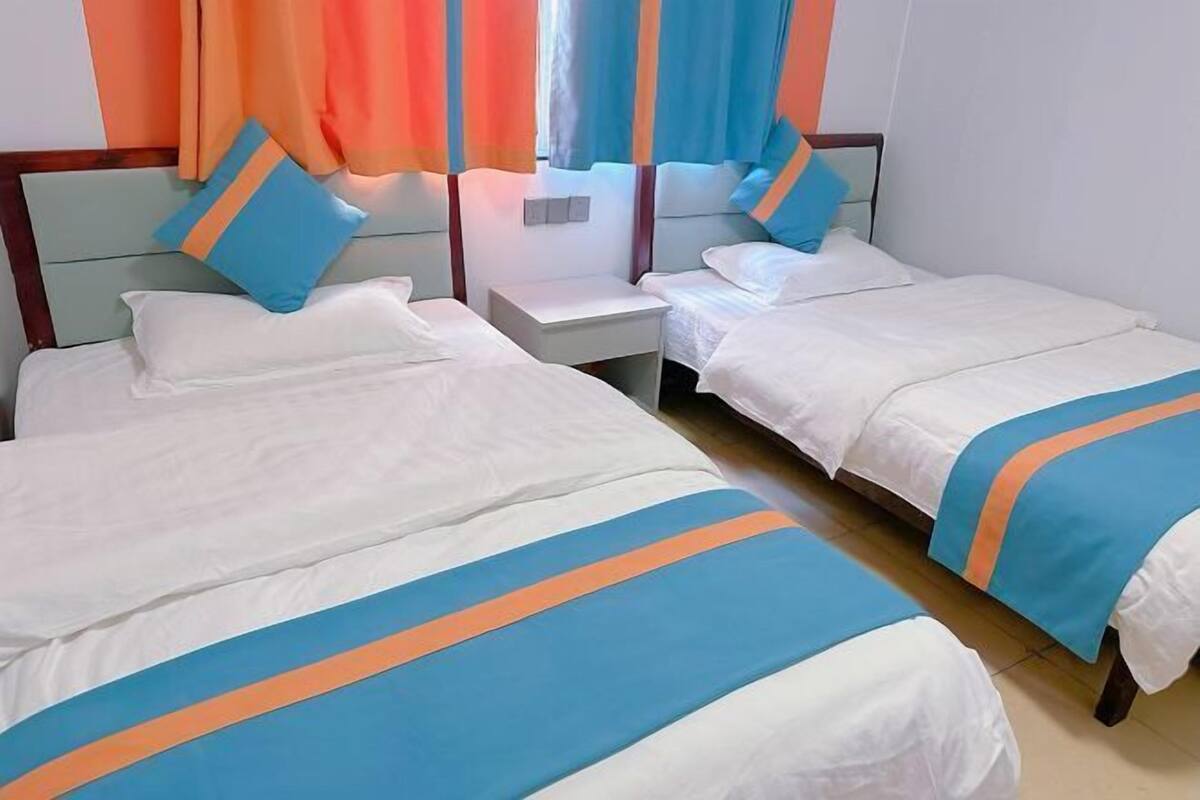 Une chambre d’hôtel avec deux lits, chacun recouvert d’une couvre-lit à rayures blanches et bleues, une table de chevet et une fenêtre avec des rideaux.