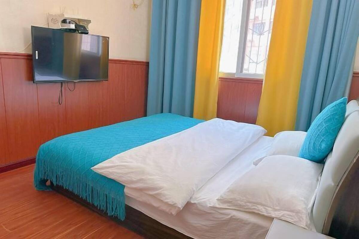 Une chambre d’hôtel avec un lit, un téléviseur fixé au mur et une fenêtre avec des rideaux.