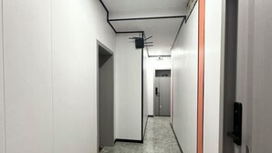 Een smalle gang met witte wanden en een marmeren vloer. Aan beide kanten bevinden zich deuren en er hangt een zwarte plafondlamp.