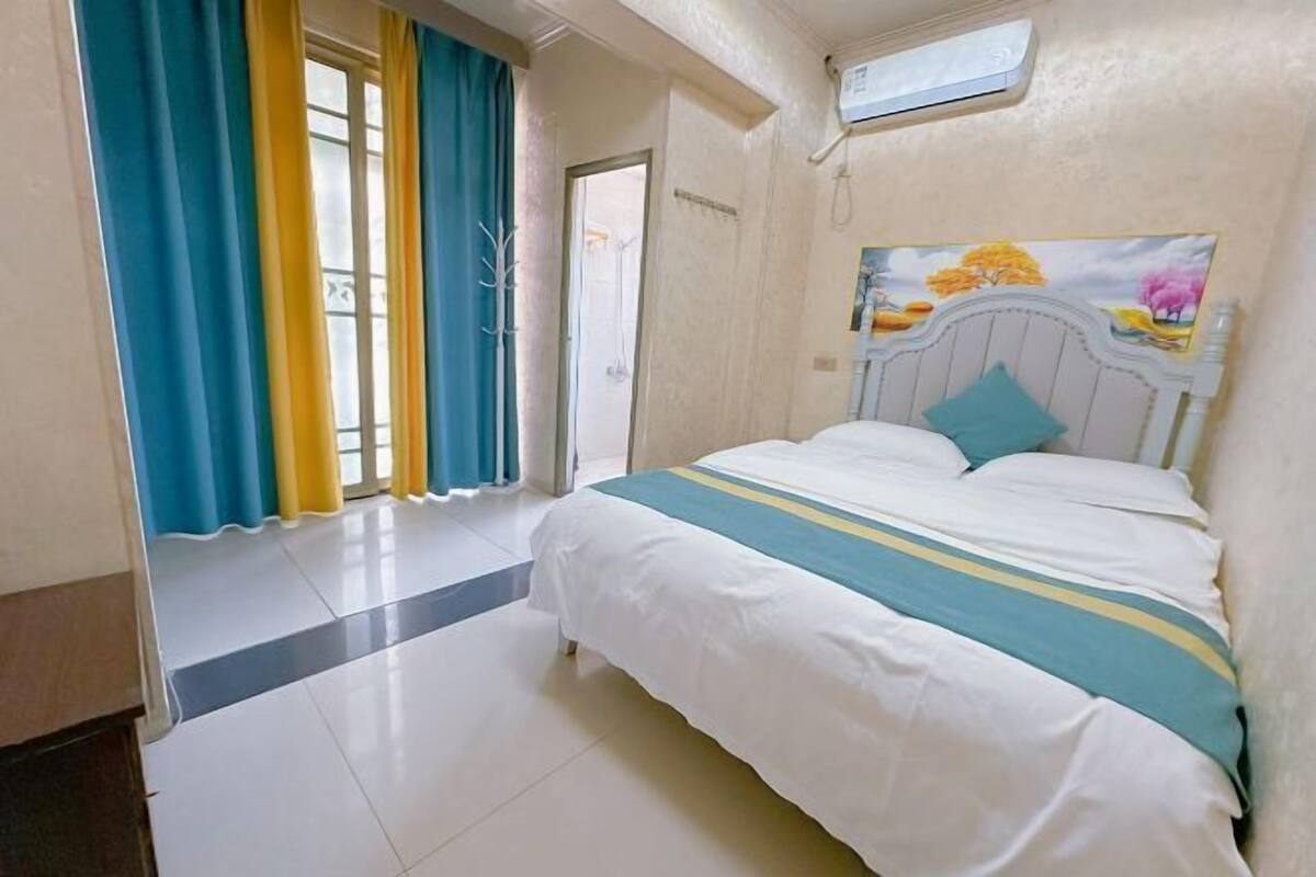 Une chambre à coucher avec un lit, des rideaux, un tableau accroché au mur et une fenêtre.