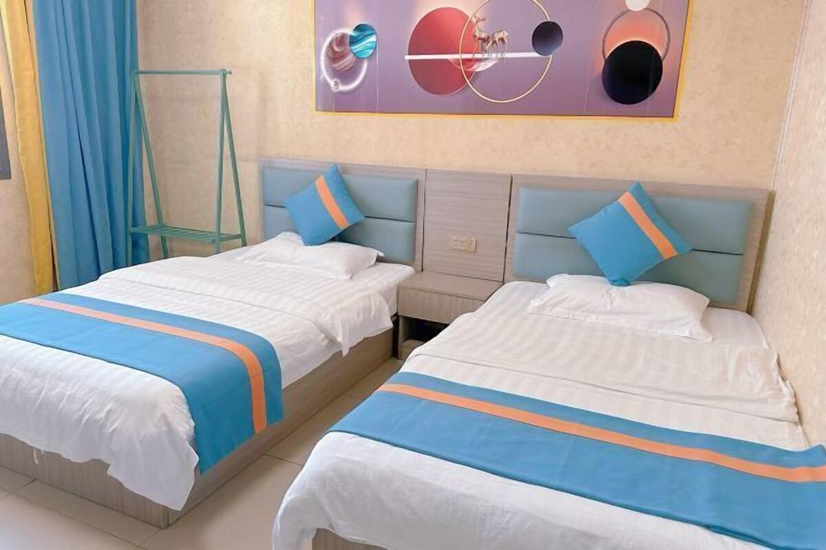 Une chambre d’hôtel avec deux lits, chacun recouvert d’une couvre-lit à rayures bleues et oranges, doté d’une tête de lit bleu clair et orné d’une œuvre d’art au-dessus des lits.